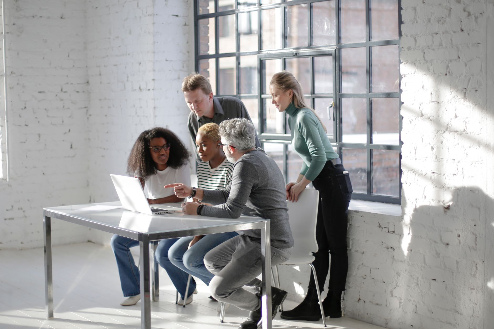 Diverse expressive coworkers sitting at a table and looking at a laptop screen while working on a project together